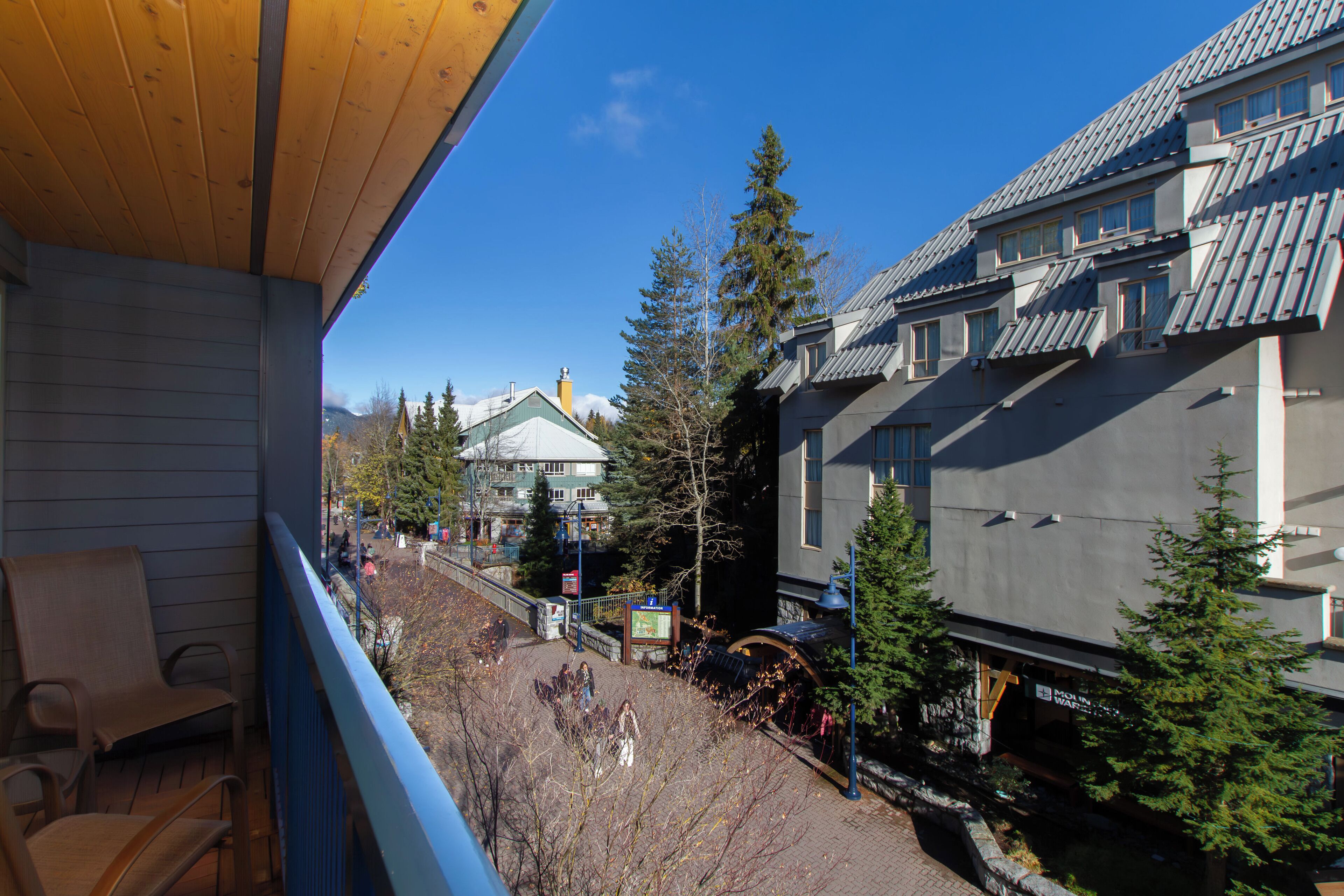 A balcony with wooden chairs, a view of a town with buildings and trees, and a clear blue sky.