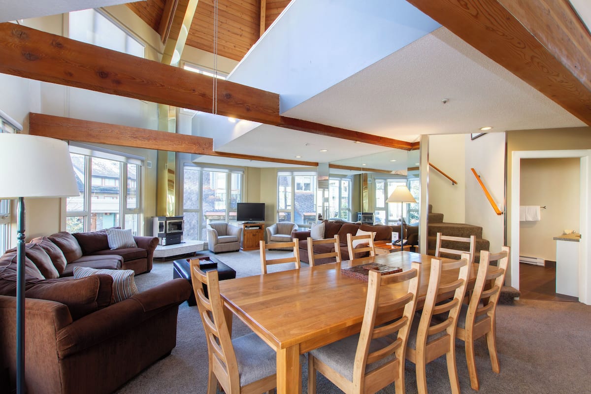 A spacious living area with a wooden dining table, multiple sofas, and a television.