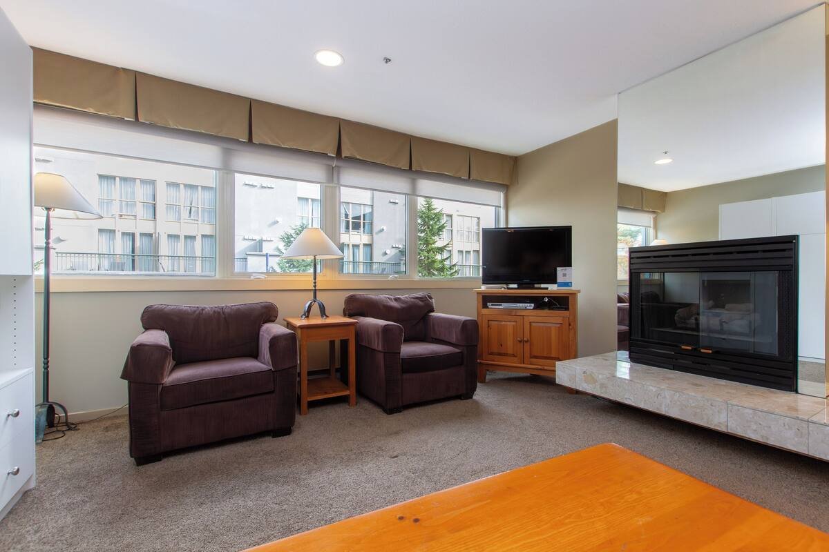 A modern living room with a fireplace, two armchairs, a coffee table, and a television.
