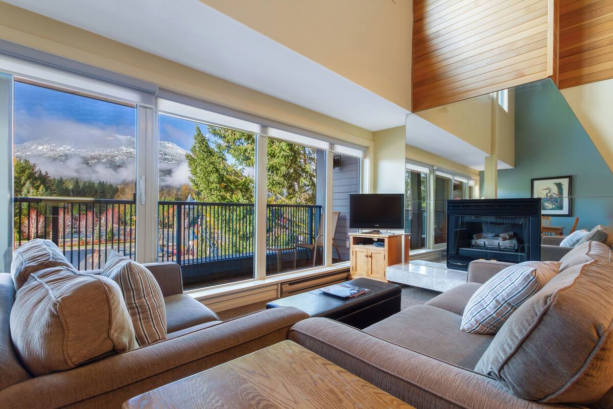 A modern living room with a large window, a fireplace, and a sofa.