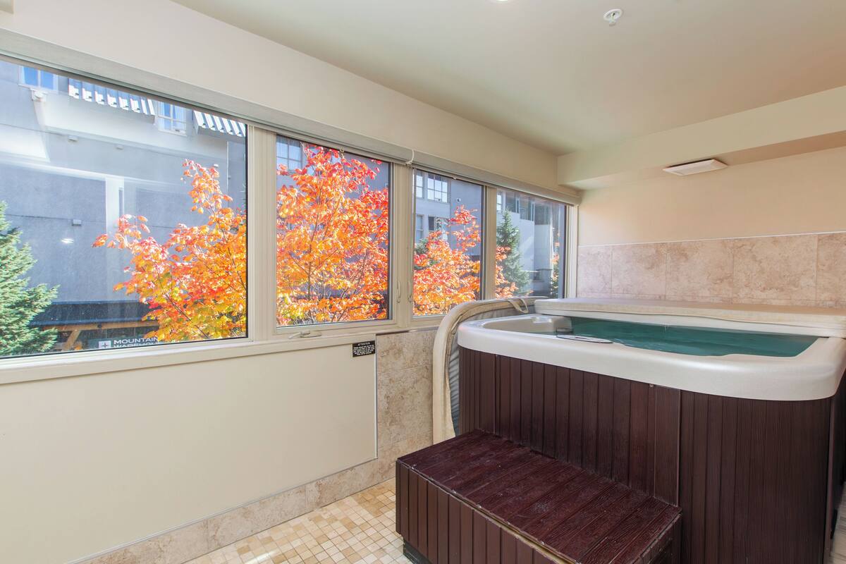 A bathroom with a large window, a hot tub, and a wooden bench.