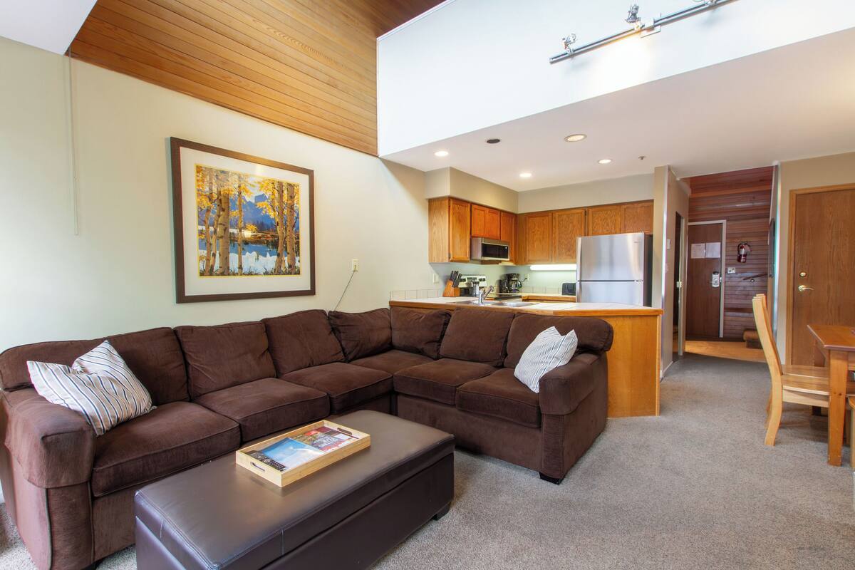 A living room with a brown sectional sofa, a wooden coffee table, and a painting on the wall.