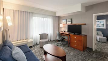 Habitación de hotel con sofá, escritorio con computadora, una silla y televisor.