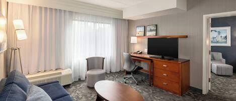 A hotel room with a sofa, a desk with a computer, a chair, and a TV.