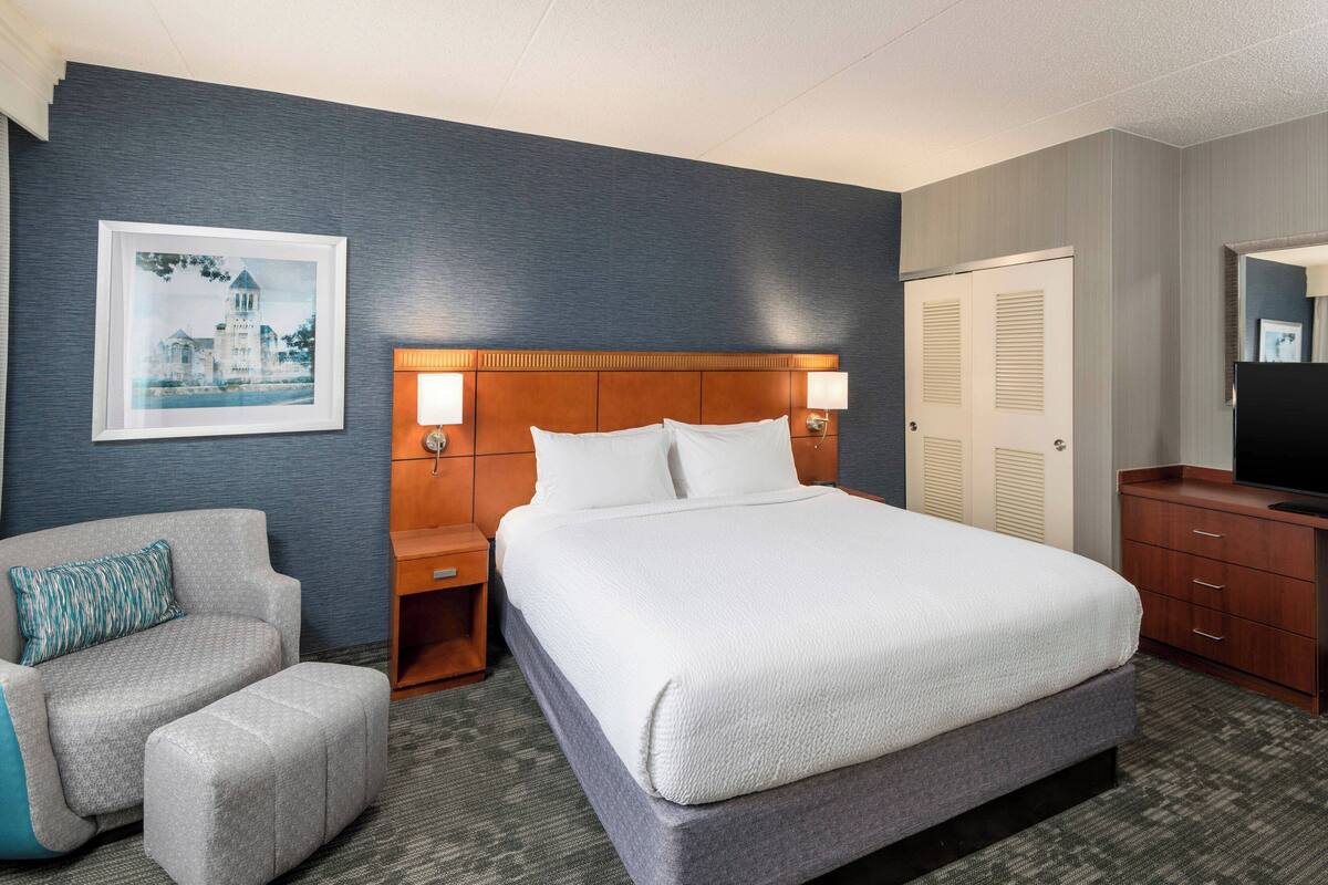 Een hotelkamer met een groot bed, een stoel, een nachtkastje, een dressoir en een ingelijste foto aan de muur.