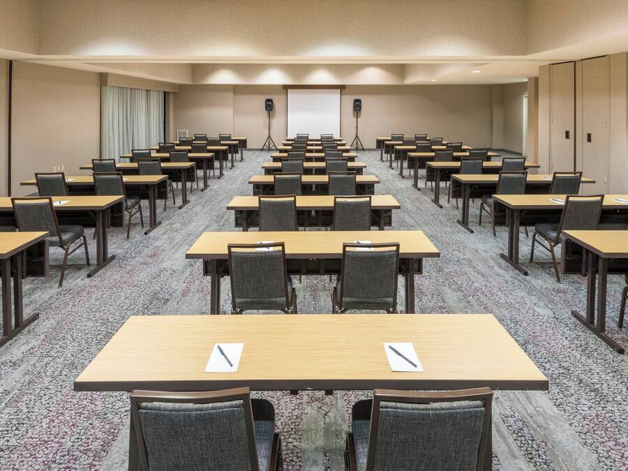 A conference room with rows of tables and chairs, a projector screen, and speakers.
