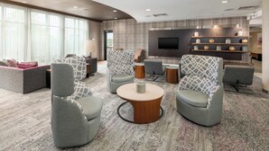 A modern lounge area with sofas, armchairs, a coffee table, and a TV mounted on the wall.