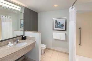 Un baño moderno con lavabo de granito, inodoro, ducha con puerta de cristal y un cuadro en la pared.