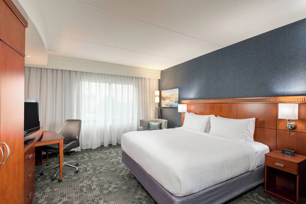 Een hotelkamer met een bed, een bureau met een computer, een stoel, een televisie en een nachtkastje met een lamp.