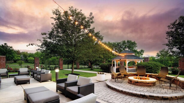 An outdoor patio area with wicker furniture, a fire pit, and string lights.