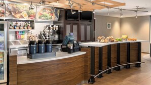 A modern coffee shop with a wooden counter, espresso machines, and a variety of baked goods.