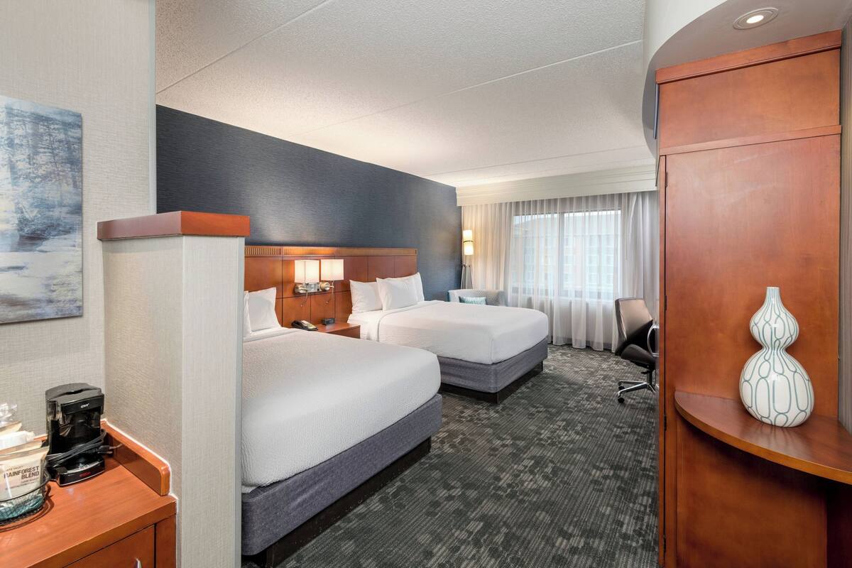 Een hotelkamer met twee bedden, een bureau met een koffiezetapparaat, een lamp en een vaas op een houten dressoir.