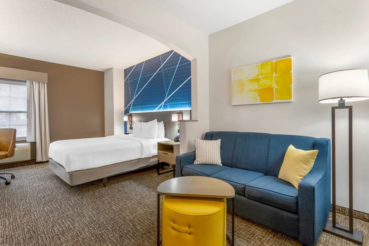 Ein Hotelzimmer mit Bett, Sofa, einem kleinen Tisch, einer Lampe und Bildern an den Wänden.