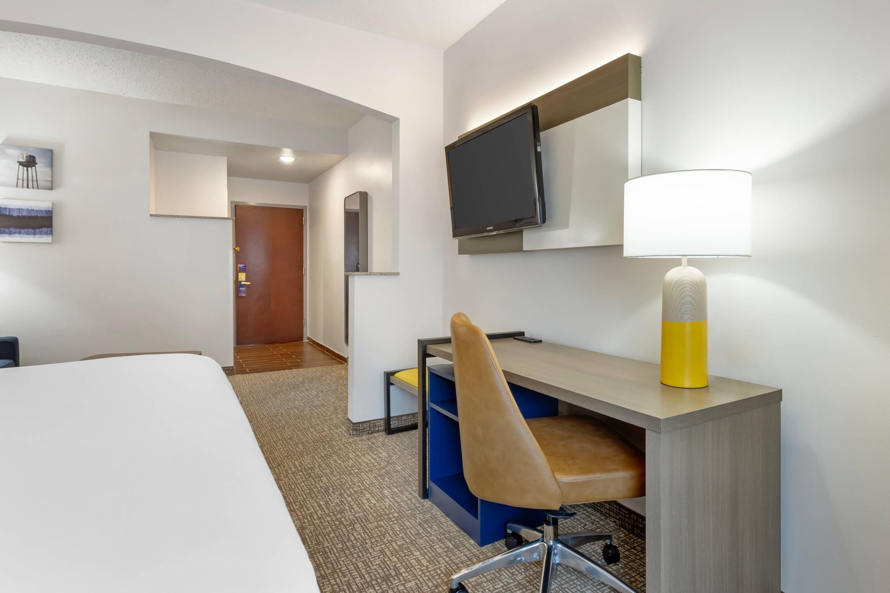 A hotel room with a bed, desk, chair, TV, and lamp.