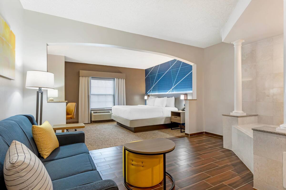 Ein Hotelzimmer mit einem Bett, einem Sofa, einem kleinen runden Tisch, einer Lampe und einem großen Fenster.