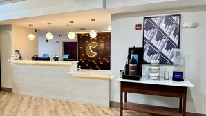 Zona de recepción de un hotel con diseño moderno, que incluye un mostrador de recepción, una máquina de café y un detector de incendios instalado en la pared.