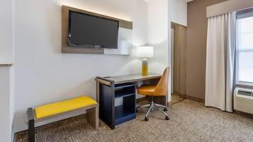 Habitación de hotel con escritorio, silla, televisión, lámpara y ventana con cortinas.