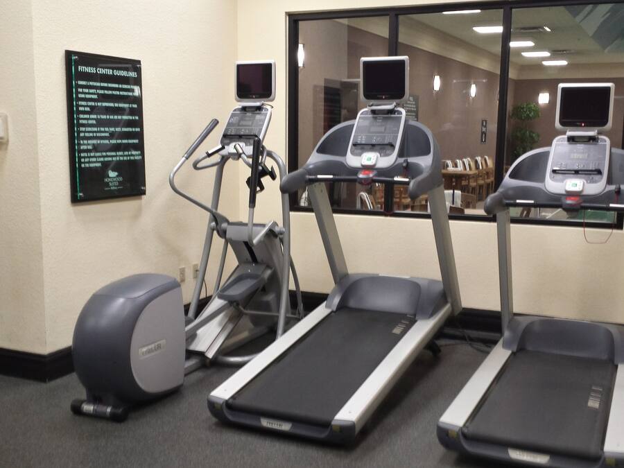 A fitness center with treadmills, an elliptical, and a stationary bike. There is a sign with guidelines on the wall.