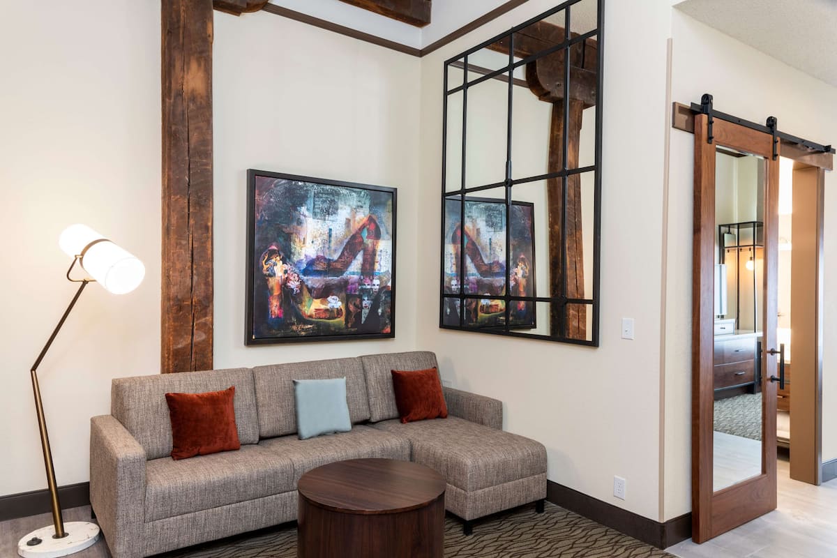 A living room with a gray sectional sofa, a round wooden coffee table, and two abstract paintings on the wall.