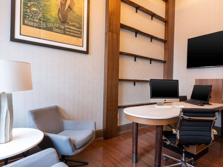 Ein Hotelzimmer mit Schreibtisch, zwei Stühlen, einer Lampe, einem Fernseher und einem gerahmten Poster an der Wand.