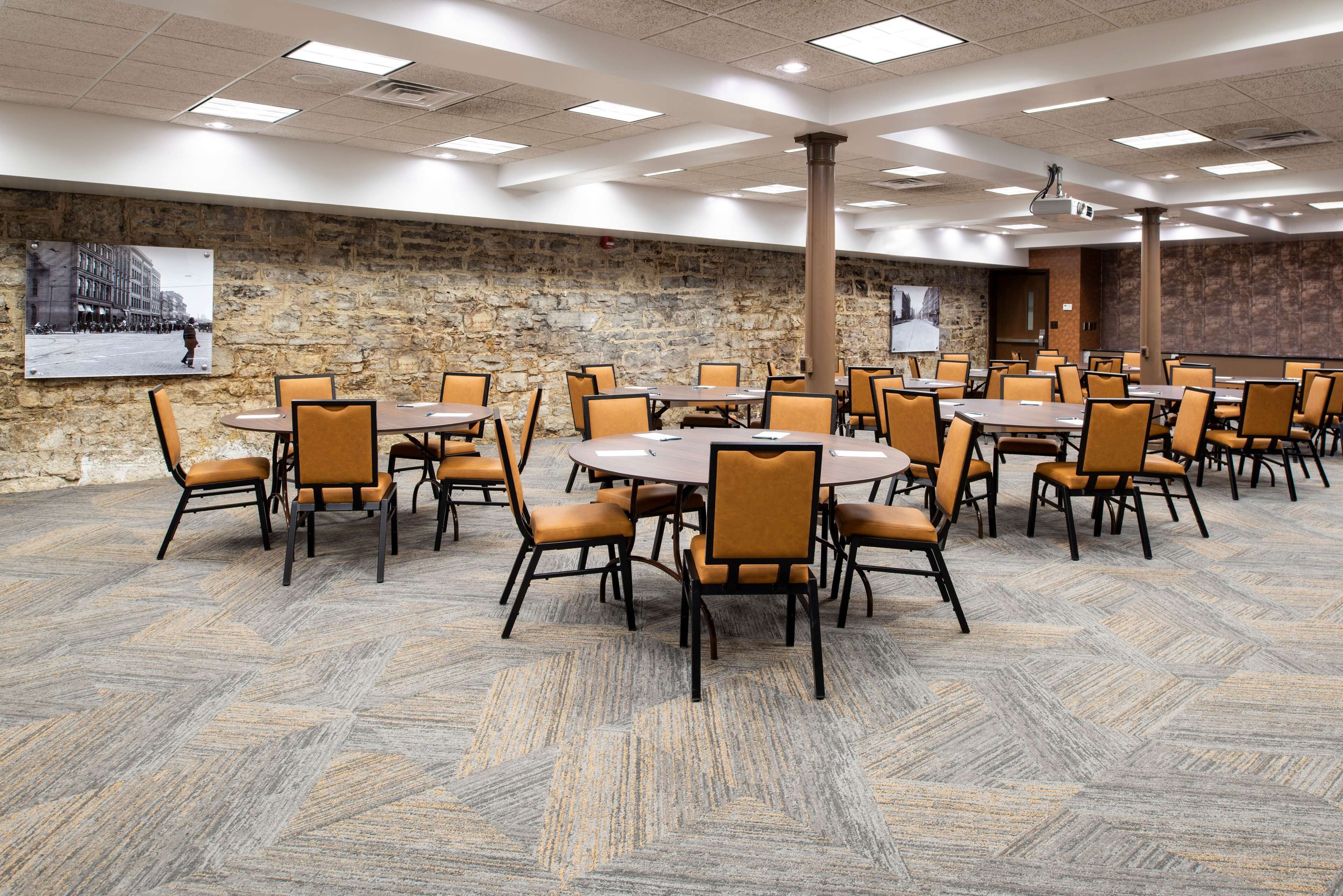 A conference room with multiple tables and chairs, stone walls, and a projector screen.