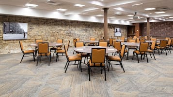 A conference room with multiple tables and chairs, stone walls, and a projector screen.