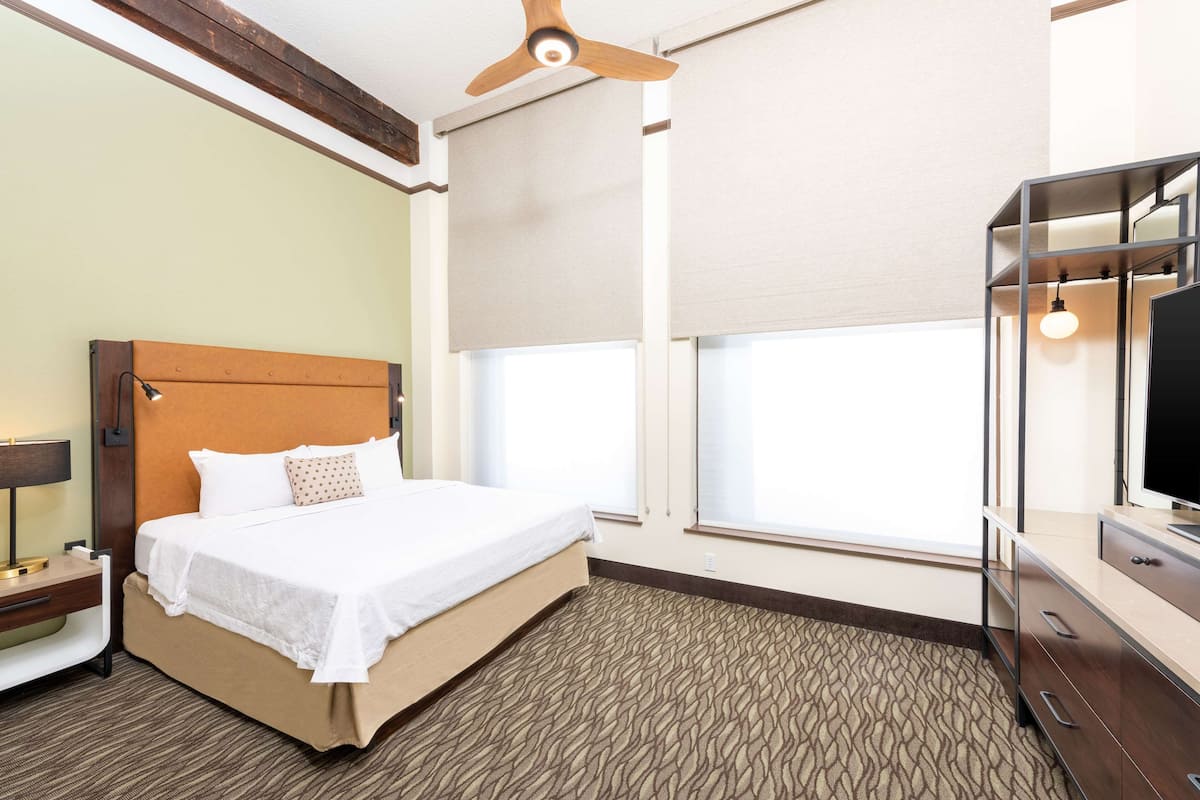 A hotel room with a bed, a desk, a television, and a ceiling fan.
