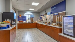 Un área de desayuno moderna con un sector de autoservicio, un refrigerador y una pantalla con el menú.