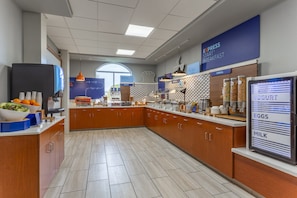 Un área de desayuno moderna con un sector de autoservicio, un refrigerador y una pantalla con el menú.