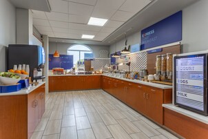 Un área de desayuno moderna con un sector de autoservicio, un refrigerador y una pantalla con el menú.