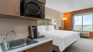 A hotel room with a kitchenette, a bed, a window with a view, and a bedside table with a lamp. - Holiday Inn Express Hotel & Suites Rockford-Loves Park by IHG (Loves Park)