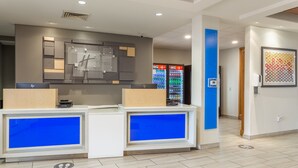A reception desk with a blue illuminated panel, a Coca-Cola refrigerator, and a framed artwork on the wall. - Holiday Inn Express Hotel & Suites Rockford-Loves Park by IHG (Loves Park)
