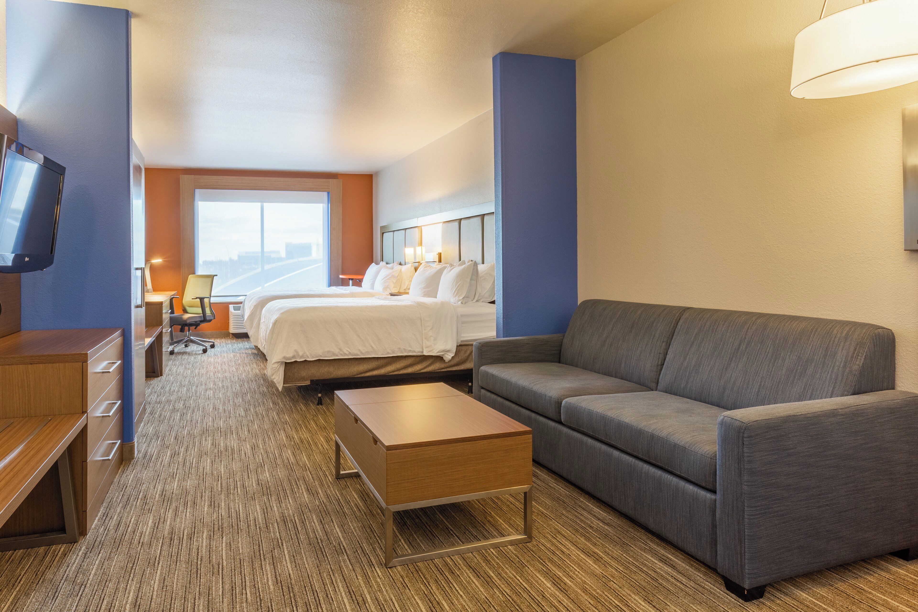 A hotel room with a bed, a sofa, a desk, and a TV.