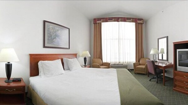 Une chambre d’hôtel avec un grand lit, deux tables de chevet, un bureau avec une chaise, une télévision et une fenêtre avec des rideaux.