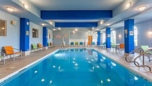 A swimming pool with blue tiles, surrounded by chairs and tables, and walls painted in blue and white. - Holiday Inn Express Hotel & Suites Rockford-Loves Park by IHG (Loves Park)