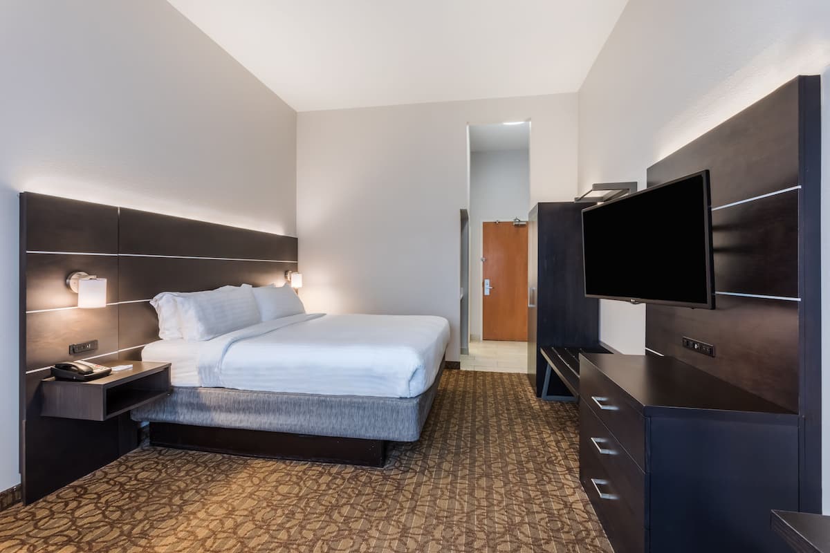 Ein Hotelzimmer mit einem großen Bett, einem Flachbildfernseher, einem Schminktisch und einem Nachttisch mit Lampe.