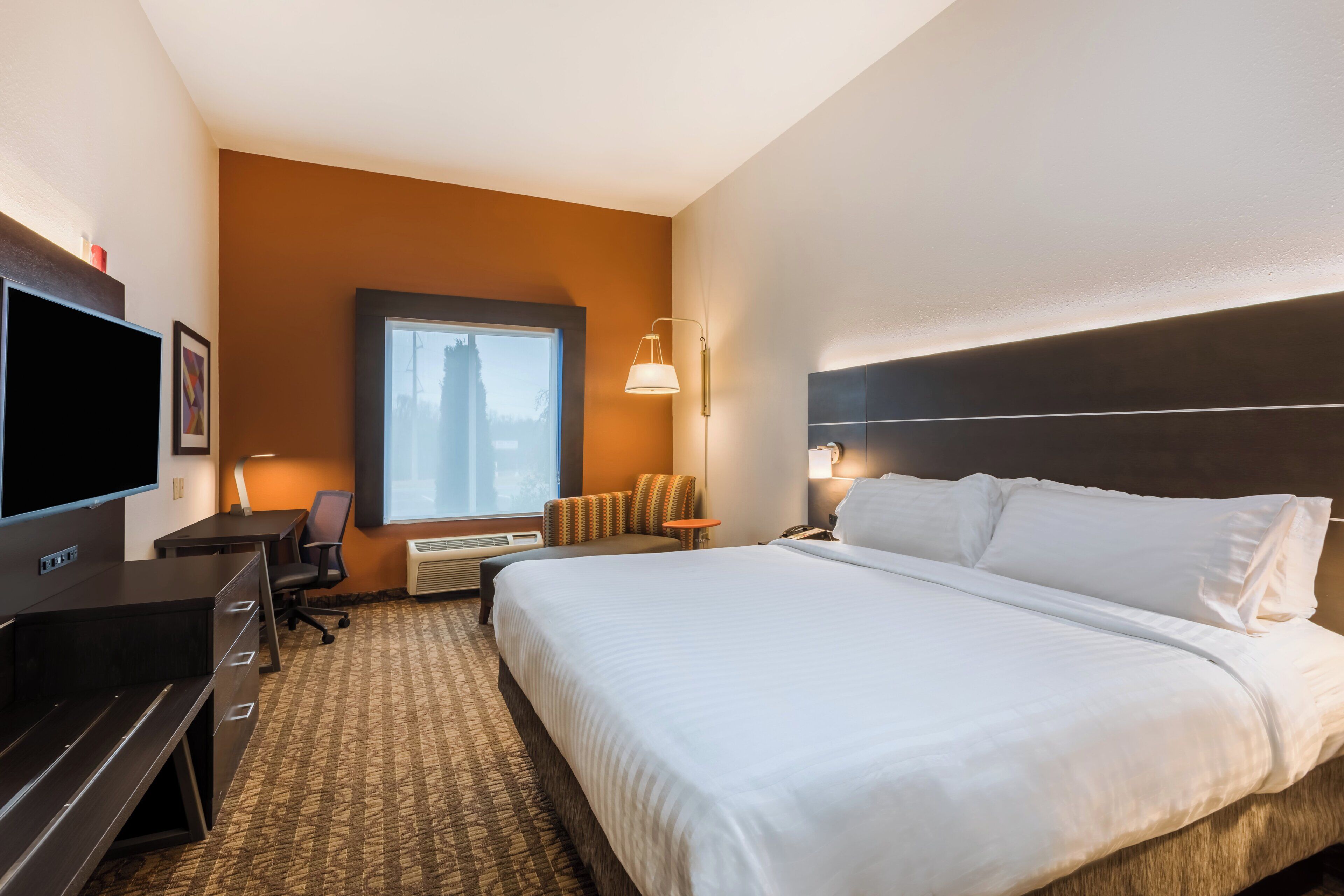 Une chambre d’hôtel avec un lit, un bureau, une chaise, une télévision et une fenêtre.