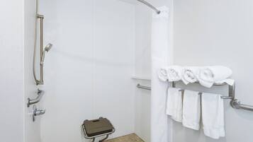 A shower with a handheld showerhead, a handheld shower attachment, and a towel rack with towels.
