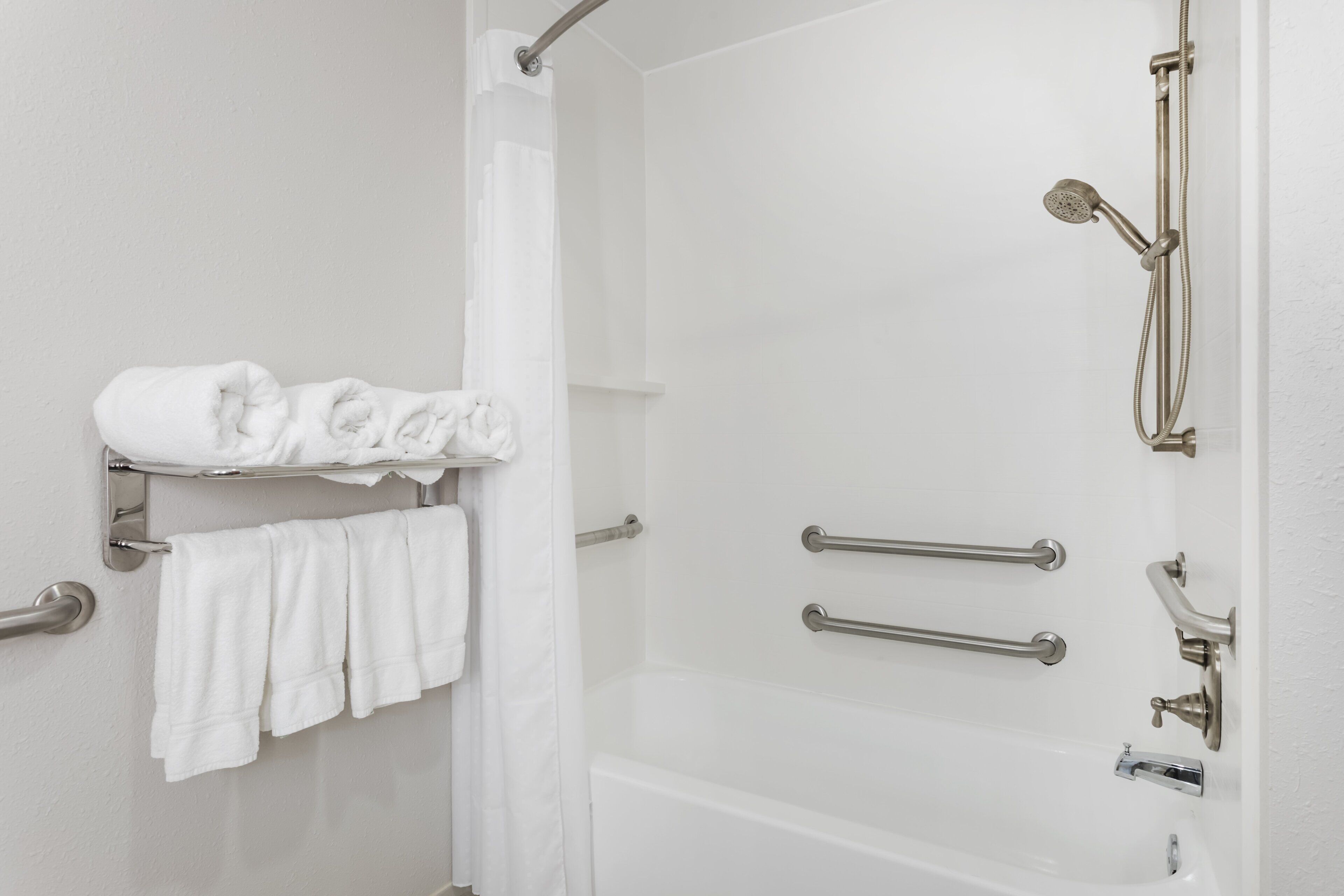 A bathroom with a shower, a towel rack with folded towels, and a grab bar.