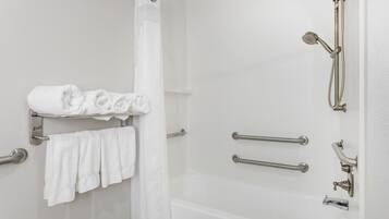 A bathroom with a shower, a towel rack with folded towels, and a grab bar.
