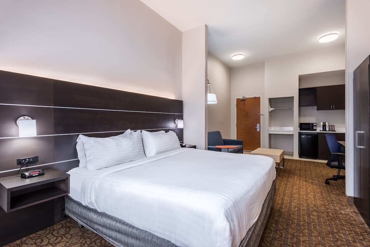 Ein Hotelzimmer mit einem großen Bett, Nachttischen, einem Schreibtisch, einem Sessel und einer Küchenzeile.