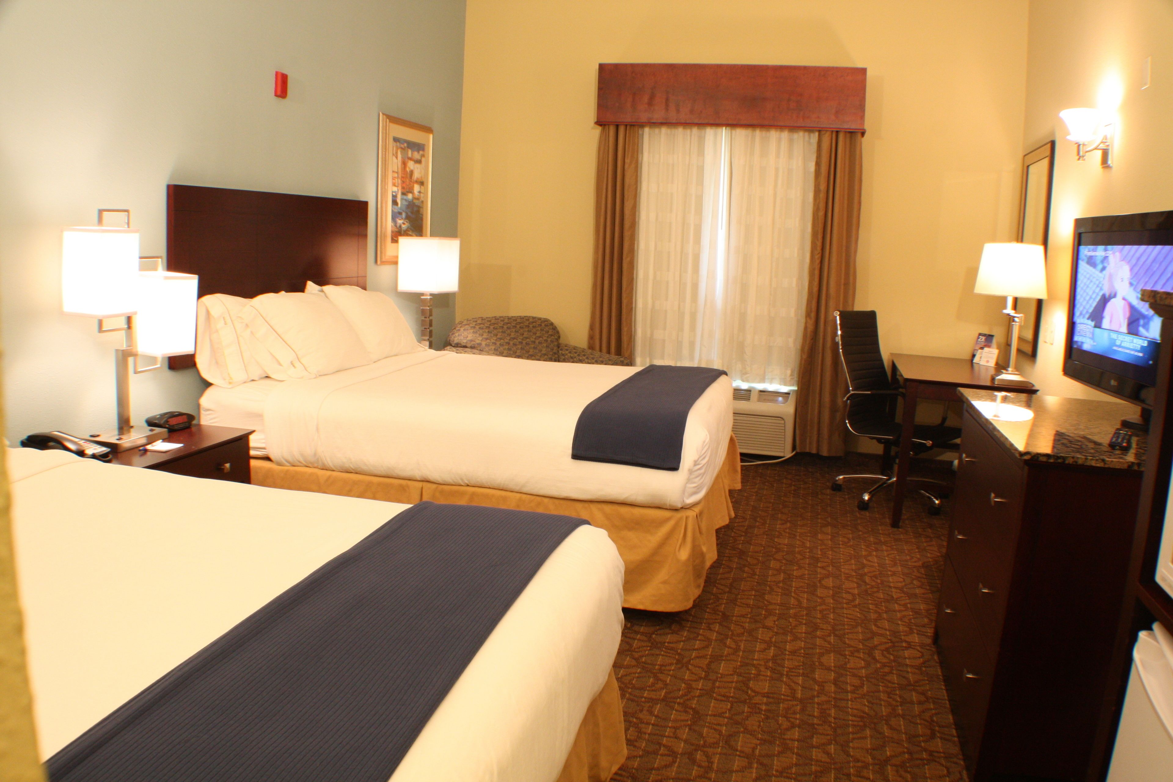 A hotel room with two beds, a desk, a television, and a chair.