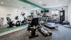 Ein Fitnessraum mit Cardiogeräten, Kurzhanteln und einer Spiegelwand.