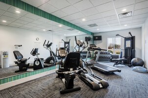 Un gimnasio con máquinas de cardio, pesas libres y un espejo grande.