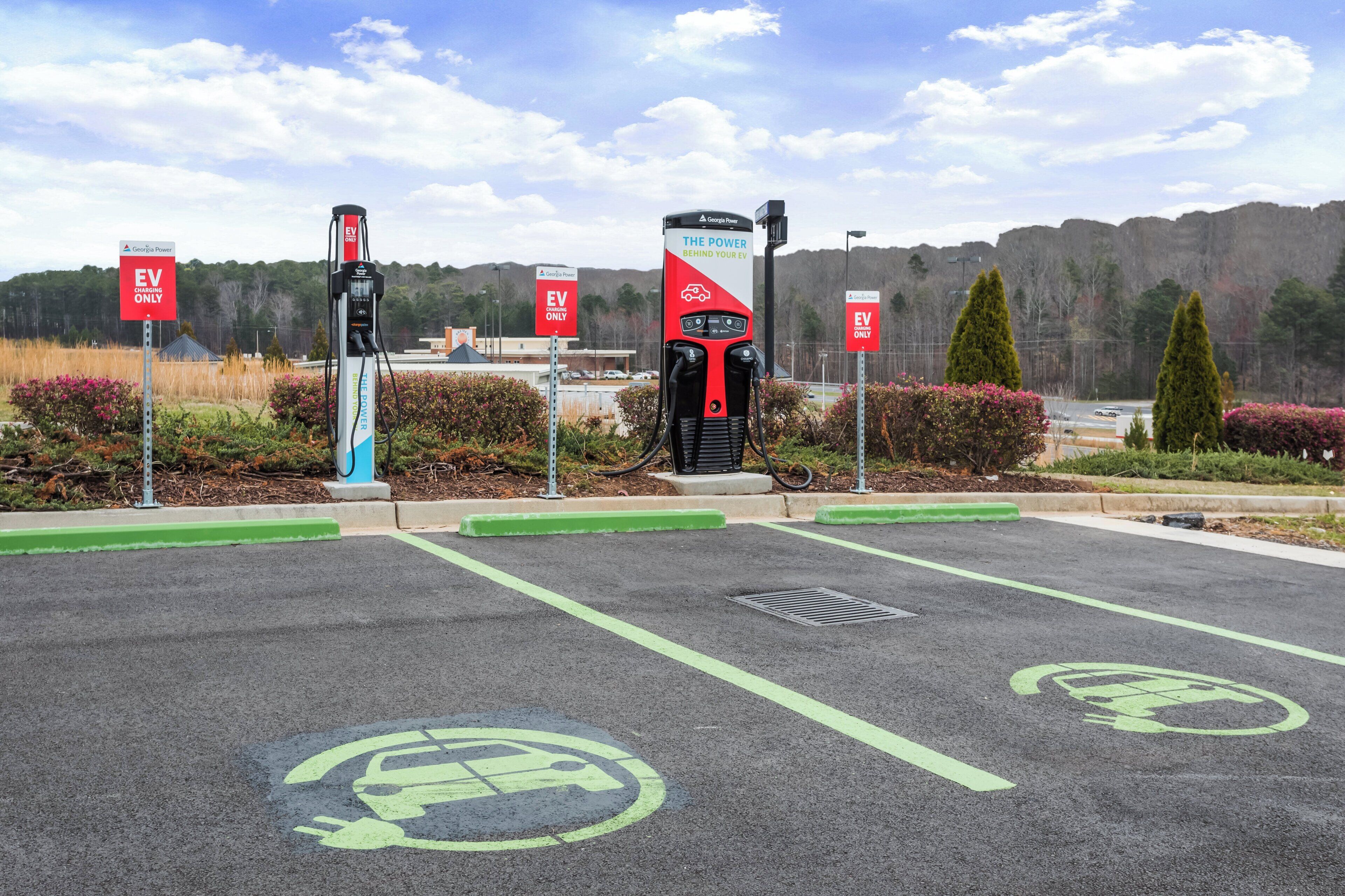 Un área de estación de carga para vehículos eléctricos con múltiples puntos de carga y señalización que indica estacionamiento 'SOLO VEHÍCULOS ELÉCTRICOS'.