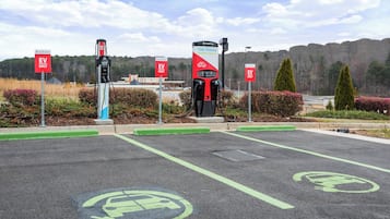 Un área de estación de carga para vehículos eléctricos con múltiples puntos de carga y señalización que indica estacionamiento 'SOLO VEHÍCULOS ELÉCTRICOS'.