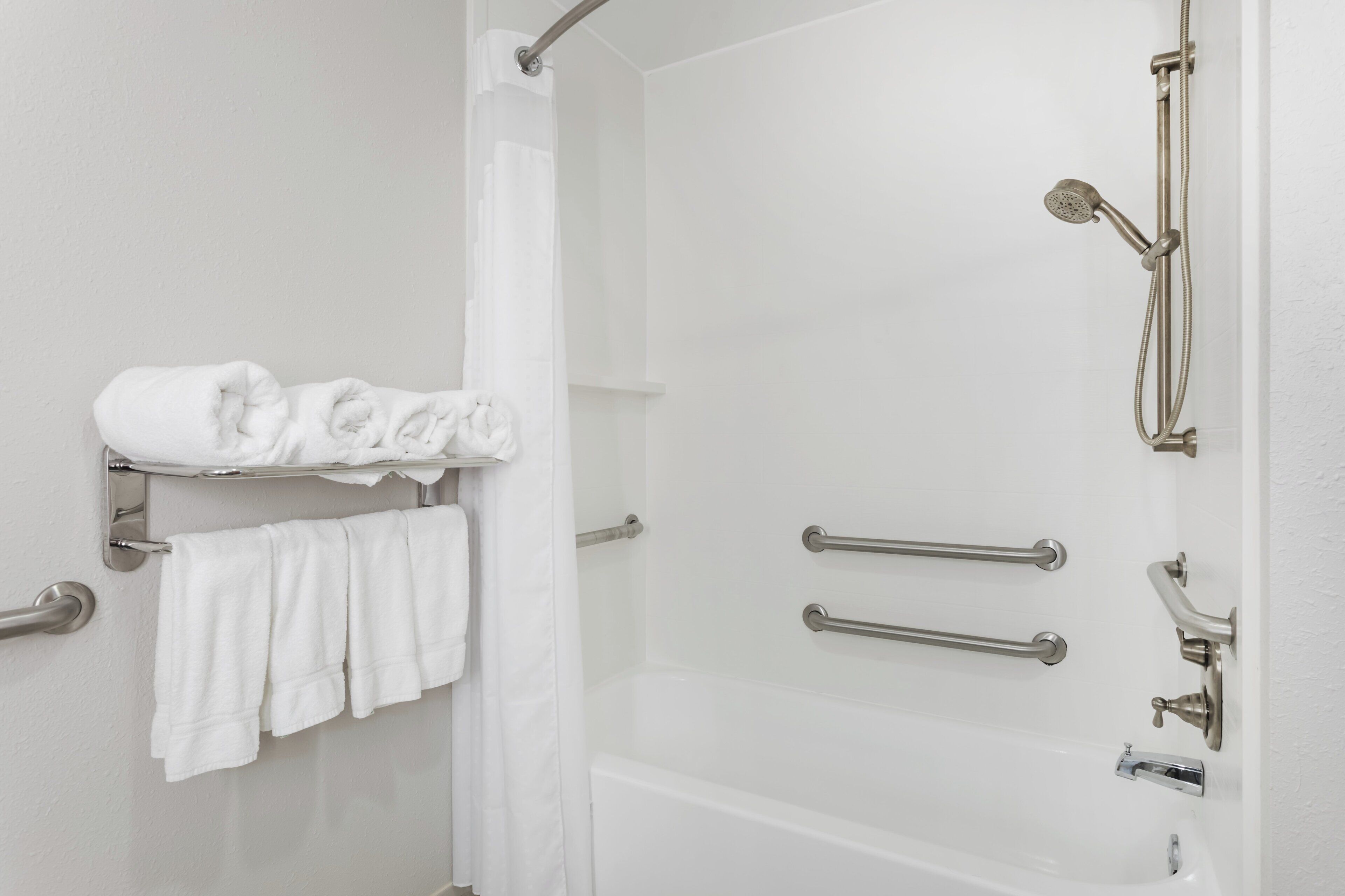 A bathroom with a shower, a toilet, and a towel rack with folded towels.