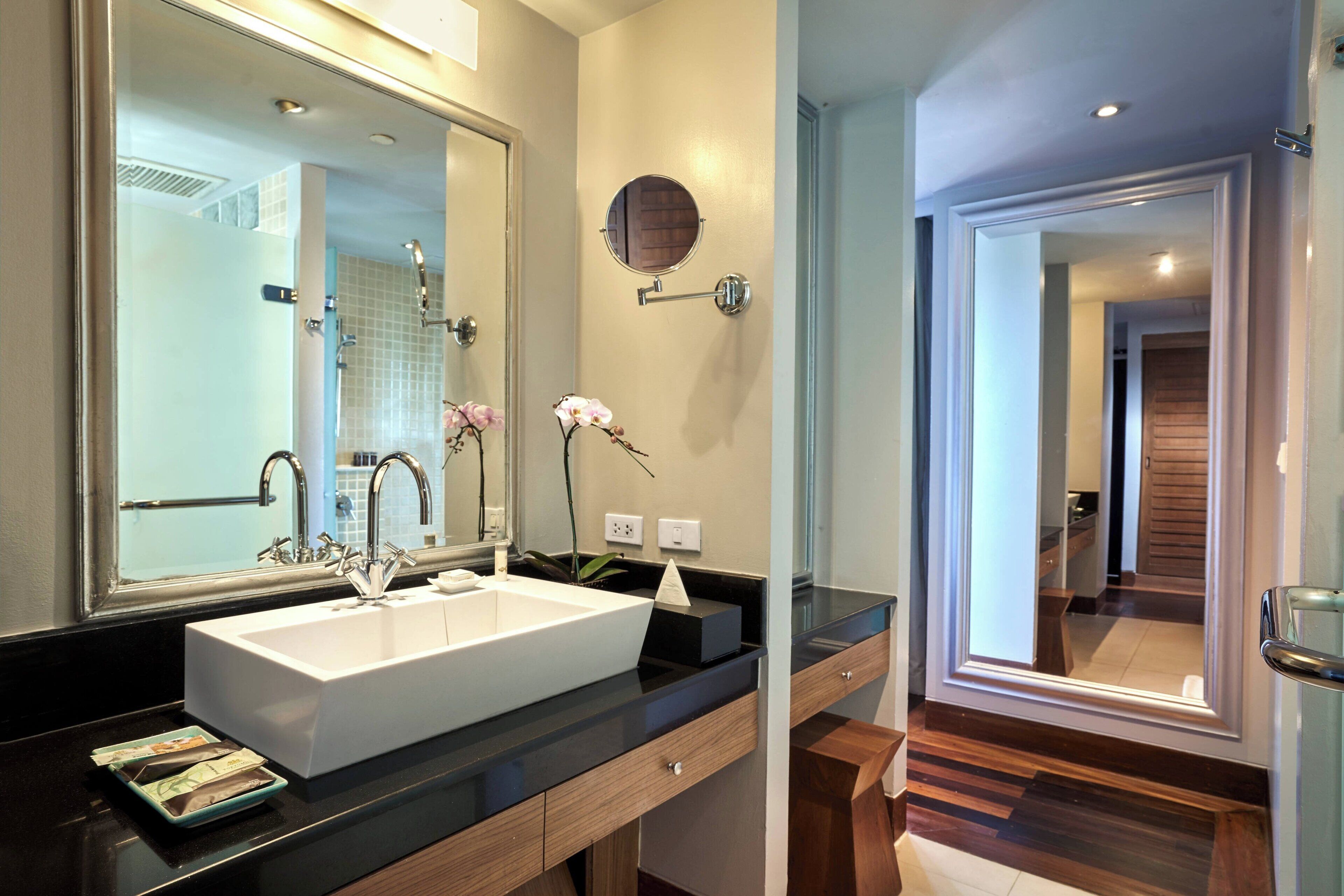 A modern bathroom with a large mirror, white sink, and wooden vanity.