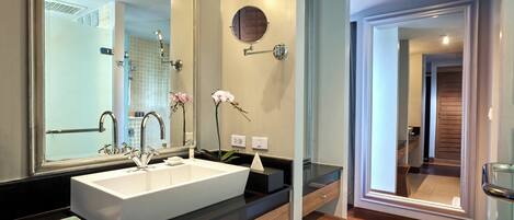 A modern bathroom with a large mirror, white sink, and wooden vanity.