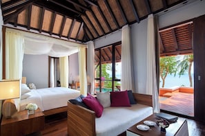 A bedroom with a bed, a sofa, a nightstand, and a view of the ocean.